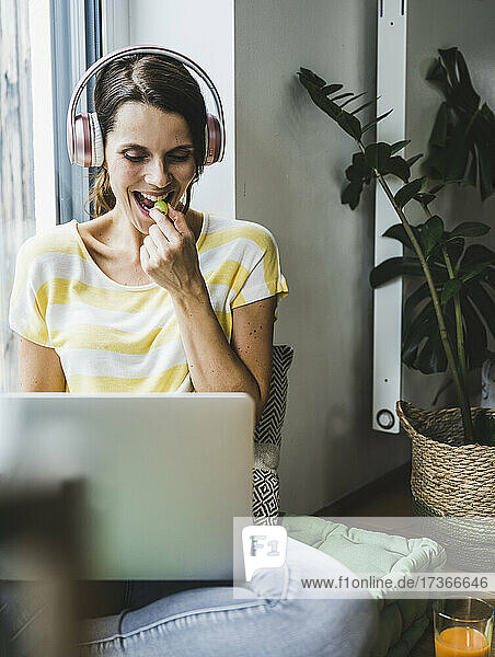 Woman eating grape while using laptop at home