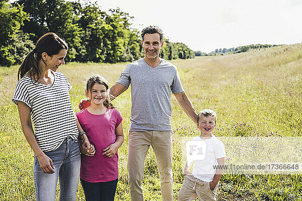 Smiling parents standing with children at meadow during sunny day