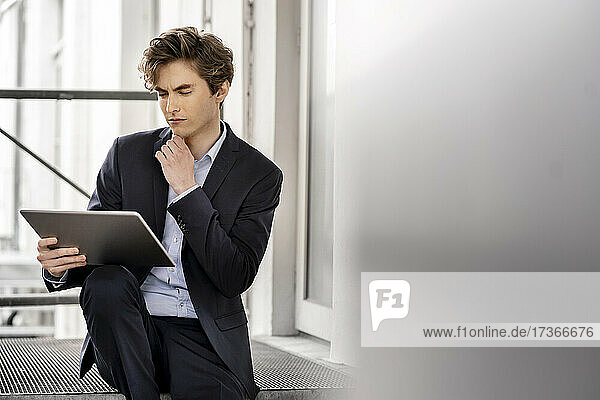 Thoughtful male professional with hand on chin looking at digital tablet
