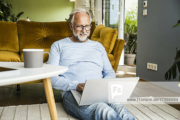 Mann benutzt Laptop  während er im Wohnzimmer auf dem Boden sitzt
