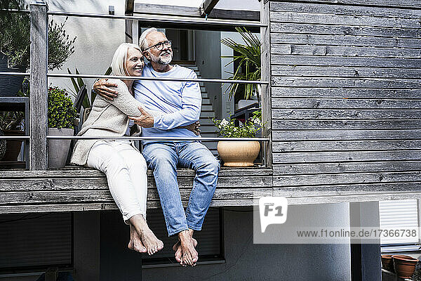 Nachdenkliches Paar  das sich umarmt  während es zusammen auf dem Balkon sitzt