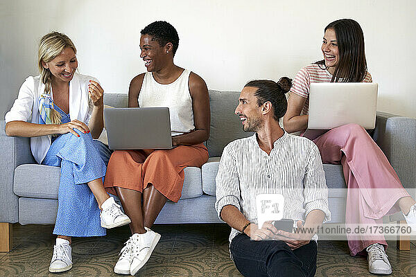 Fröhliche männliche und weibliche Mitarbeiter mit Laptops und Mobiltelefonen im Büro