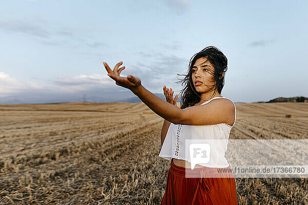 Woman stretching hand while standing at field during sunset