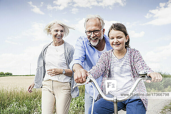 Lächelnde Großeltern spielen mit ihrer Enkelin  die Fahrrad fährt