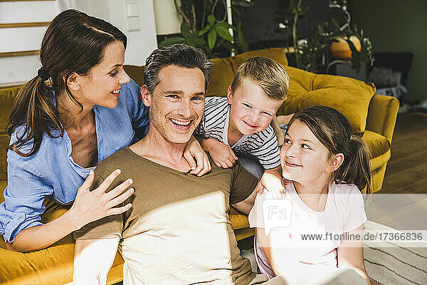 Frau schaut auf lächelnden Mann  der mit Kindern in der Nähe des Sofas zu Hause sitzt