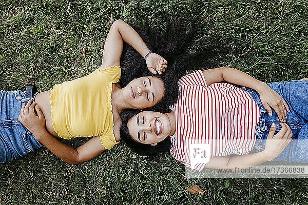 Glückliche junge Frau  die mit ihrer Freundin im Gras im Park liegt