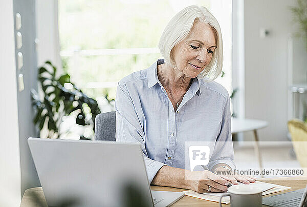 Weibliche Fachkraft beim Schreiben auf Papier im Home Office