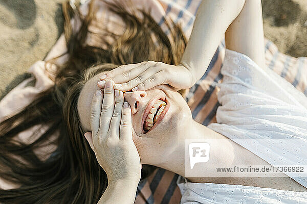 Glückliche Frau  die ihre Augen bedeckt  während sie auf einem Strandtuch liegt
