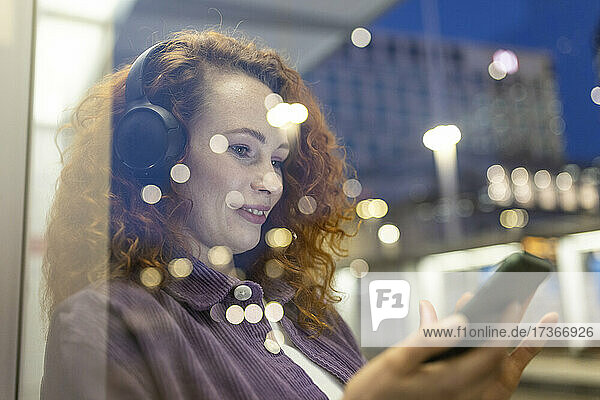 Young woman using mobile phone behind glass