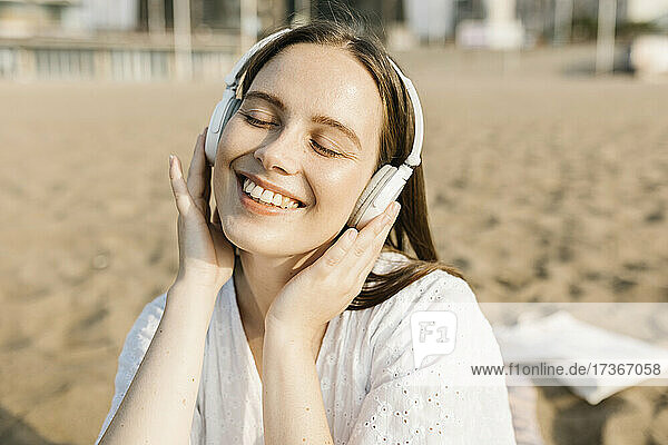 Glückliche Frau hört Musik über Kopfhörer am Strand