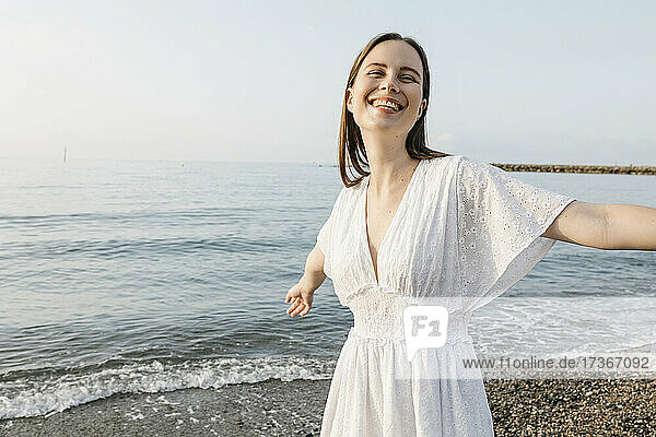 Glückliche Frau mit ausgestreckten Armen am Strand stehend