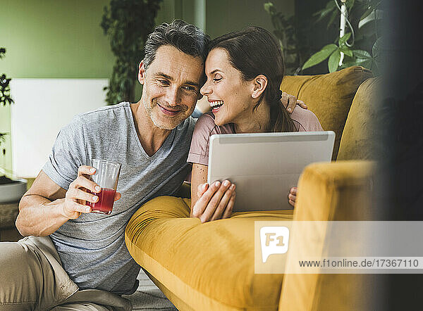 Frau mit digitalem Tablet  die einen Mann ansieht  der ein Saftglas zu Hause hält