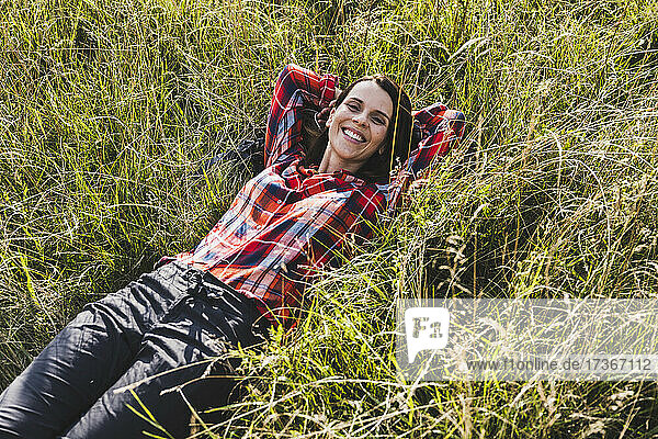 Smiling woman with hands behind head lying on grass