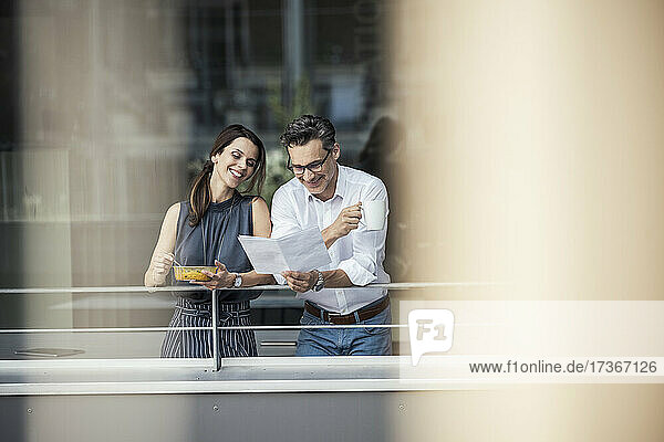 Männliche und weibliche Kollegen prüfen Dokumente  während sie auf dem Balkon des Büros stehen