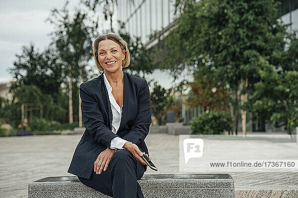 Lächelnde reife Frau mit Mobiltelefon auf einer Bank sitzend
