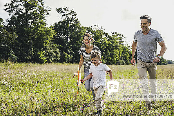 Eltern laufen hinter ihrem Sohn  der ein Spielzeugflugzeug im Gras hält