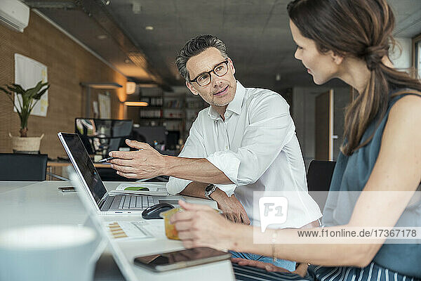 Businessman explaining to colleague while sitting at workplace
