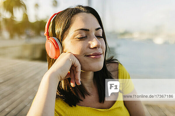 Smiling woman listening music through headphones with eyes closed