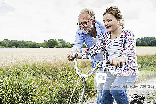 Lächelnder reifer Mann  der einem Mädchen beim Fahrradfahren auf einer Wiese hilft