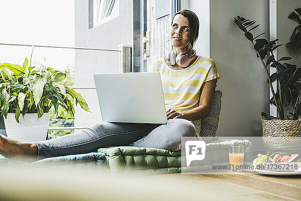 Nachdenkliche Frau  die einen Laptop benutzt  während sie zu Hause sitzt
