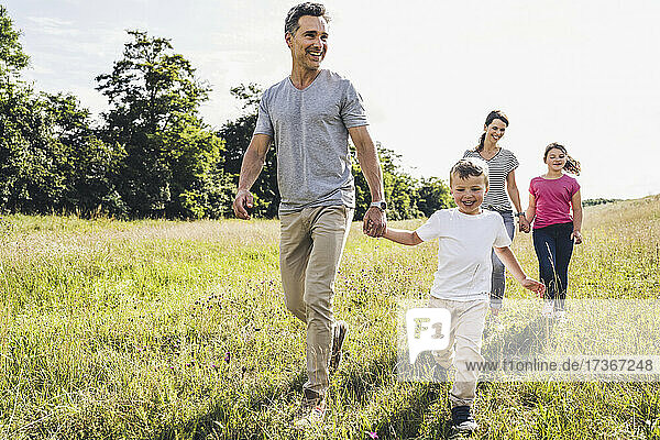 Parents holding hands of children while walking on grass during sunny day