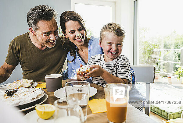 Smiling boy holding pie while having breakfast with family at home