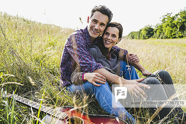 Smiling couple sitting together by guitar on grass