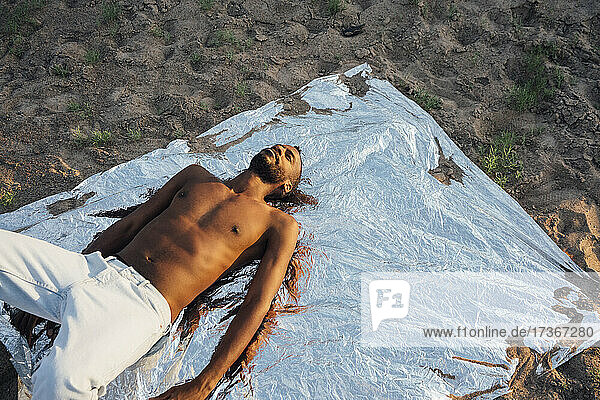 Shirtless man with eyes closed lying on aluminum foil