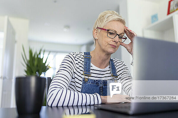 Besorgte Geschäftsfrau mit dem Kopf in der Hand  während sie im Heimbüro auf ihren Laptop schaut