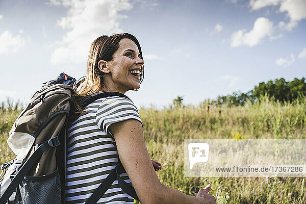 Fröhliche Frau mit Rucksack  die an einem sonnigen Tag wegschaut