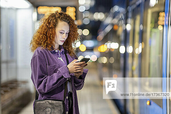 Curly haired woman using mobile phone at tram station