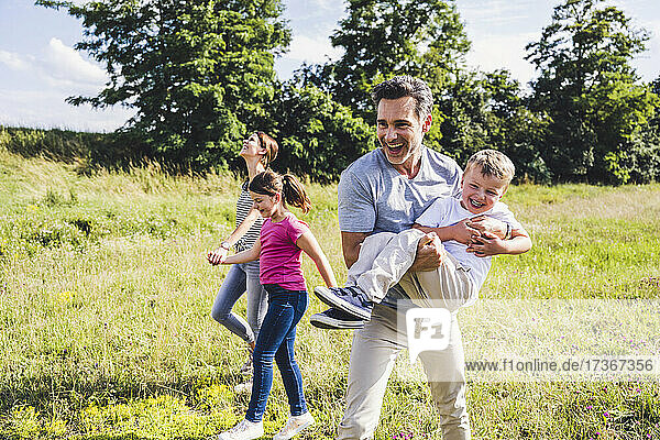 Cheerful father carrying son while walking at meadow