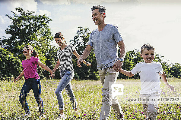 Lächelnde Familie  die sich beim Spazierengehen im Gras an den Händen hält