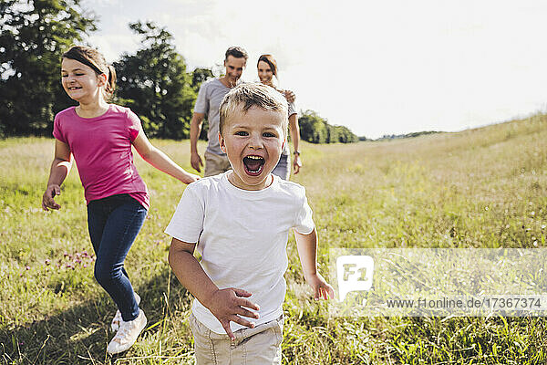 Glücklicher Junge mit offenem Mund  der an einem sonnigen Tag vor seiner Familie herläuft