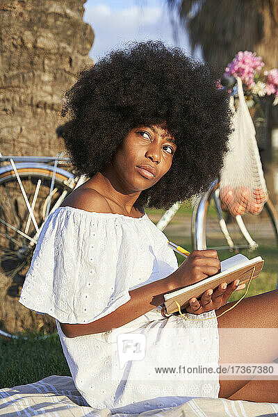 Nachdenkliche Afro-Frau  die im Park in ein Buch schreibt