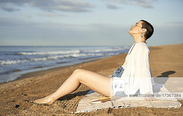 Frau entspannt auf einer Decke am Strand sitzend