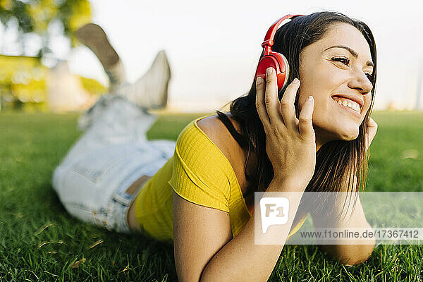 Lächelnde Frau hört Musik über Kopfhörer  während sie sich im Gras entspannt
