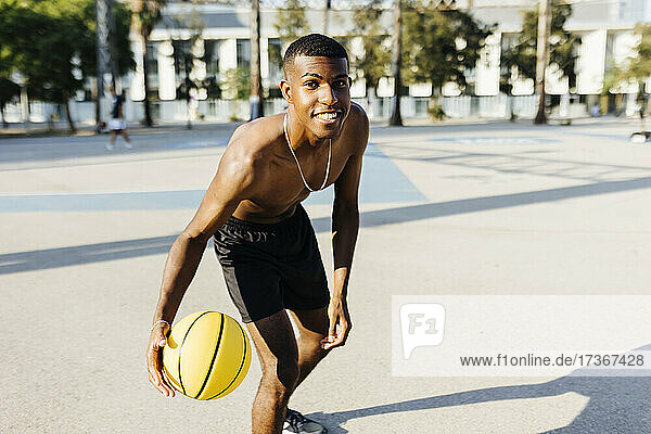 Junger Mann ohne Hemd übt Basketball auf dem Sportplatz