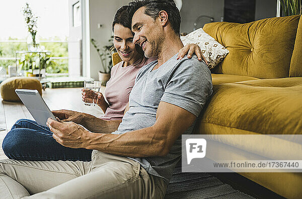 Frau hält Wasserglas  während Mann digitales Tablet zu Hause benutzt
