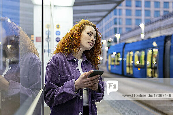 Frau mit Mobiltelefon wartet am Bahnhof auf die Straßenbahn
