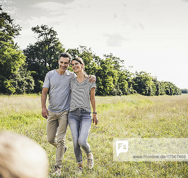 Lächelndes Paar  das an einem sonnigen Tag im Gras spazieren geht