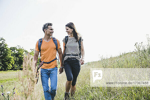 Lächelndes Paar mit Rucksäcken  das sich beim Wandern im Gras unterhält