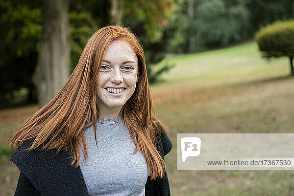 Porträt einer lächelnden jungen Frau  die in einem öffentlichen Park sitzt