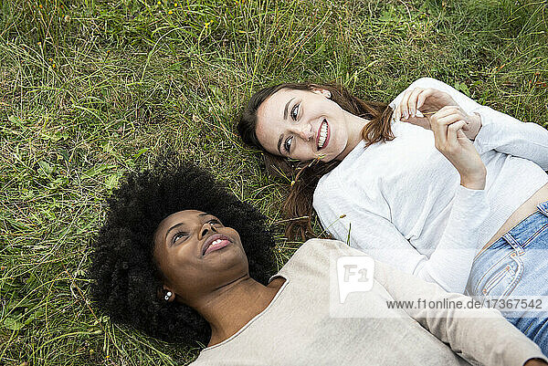 Lächelnde junge Freundinnen liegen im Park