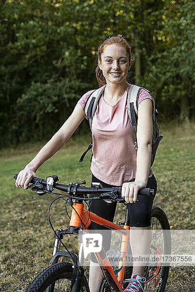 Smiling young woman sitting on bicycle in forest