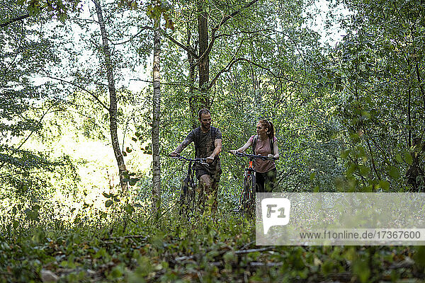 Lächelndes junges Paar geht mit Fahrrädern im Wald spazieren