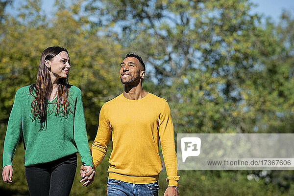 Lächelndes junges Paar geht zusammen in einem öffentlichen Park spazieren