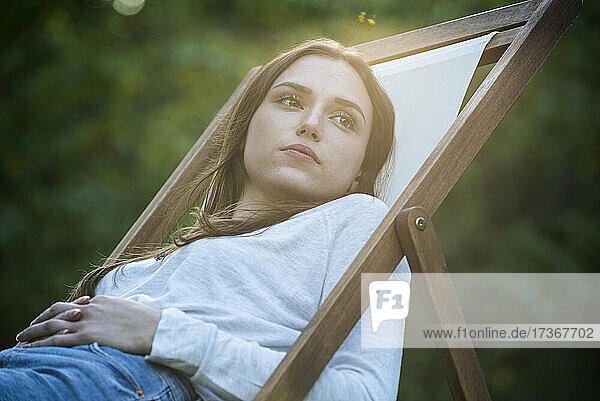Thoughtful young woman with hands on stomach leaning on chair