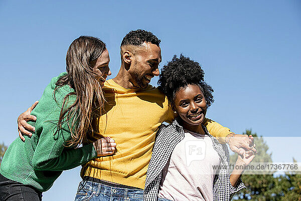 Portrait of smiling young friends standing with arm around in public park
