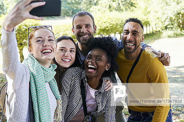 Lächelnde Frau  die ein Selfie mit ihrem Smartphone macht  während sie mit Freunden im Park steht